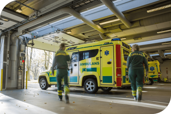 Ambulanspersonal går mot en ambulans som står i en ambulanshall